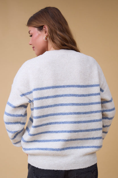 Back view of a woman wearing an oatmeal & blue stripe sweater with long sleeves and a crew neckline.