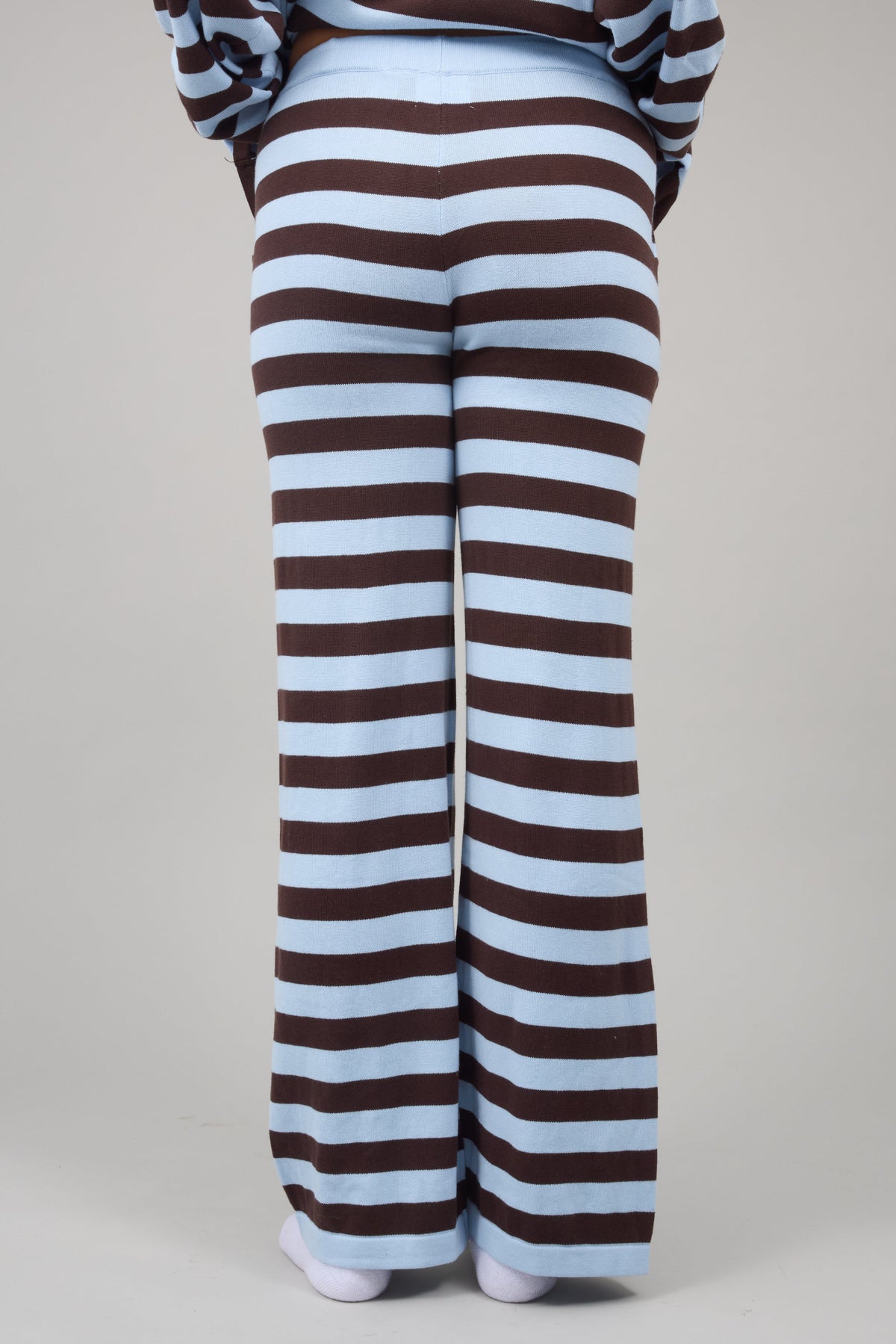 Back view of a woman wearing brown and baby blye stripe wide leg pants.