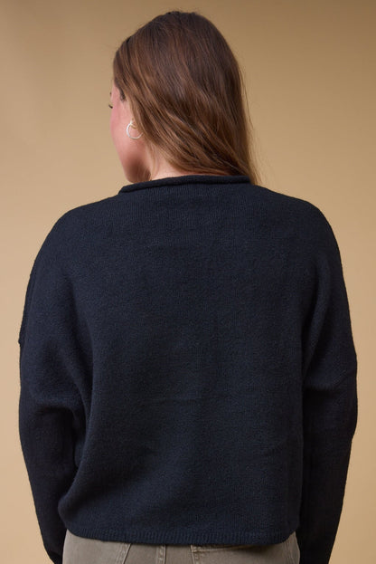 Back view of a woman wearing a long sleeve, loose fitting sweater with long sleeves.