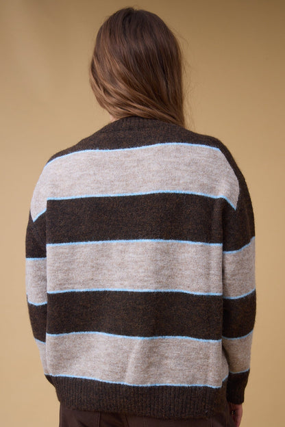Back view of a young woman wearing a tan, brown and narrow blue stripe pullover sweater with long sleeves.