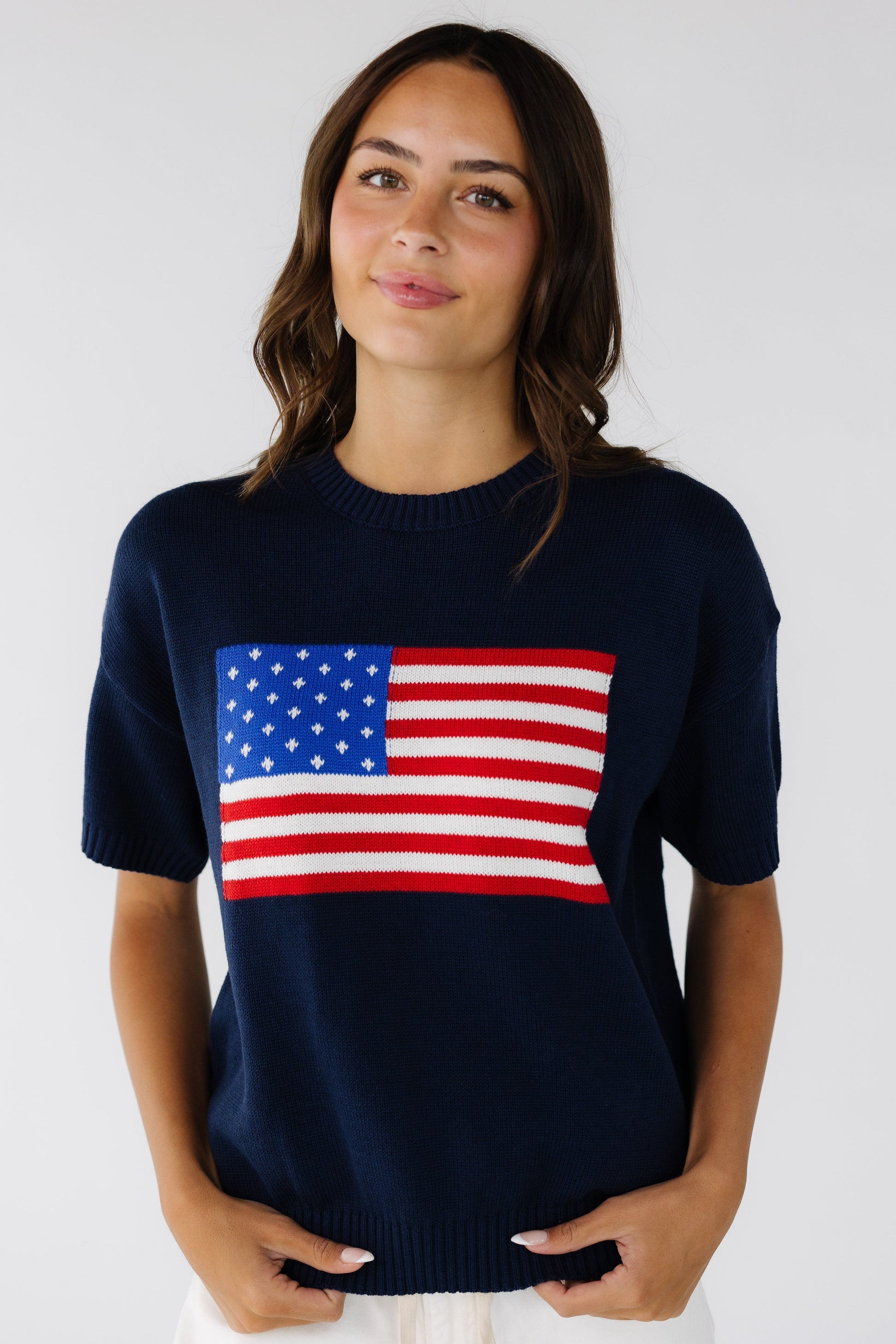 Young woman wearing a navy short sleeve sweater with a large front American flag graphic.