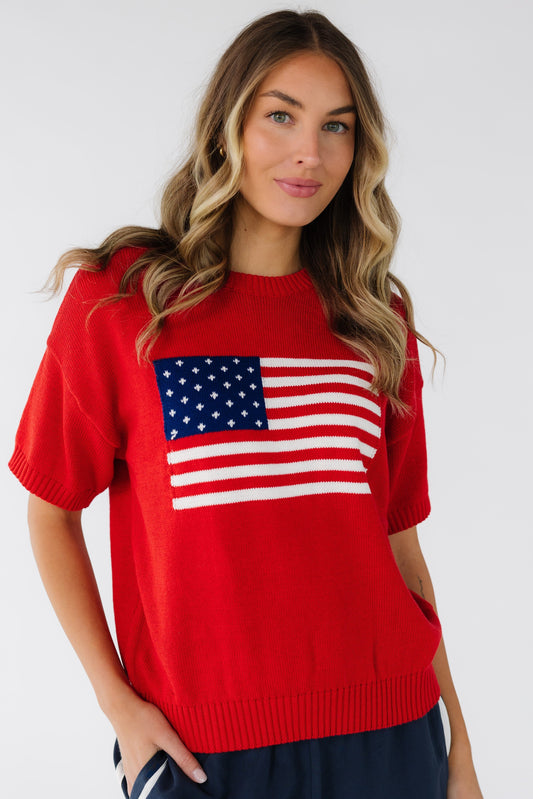 Young woman wearing a modest short sleeve sweater in red with a large front American flag graphic.