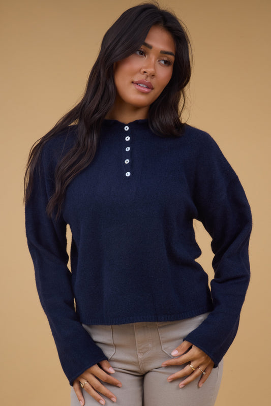 Young woman wearing a modest long sleeve sweater in navy with a rolled collar and a short button placket.
