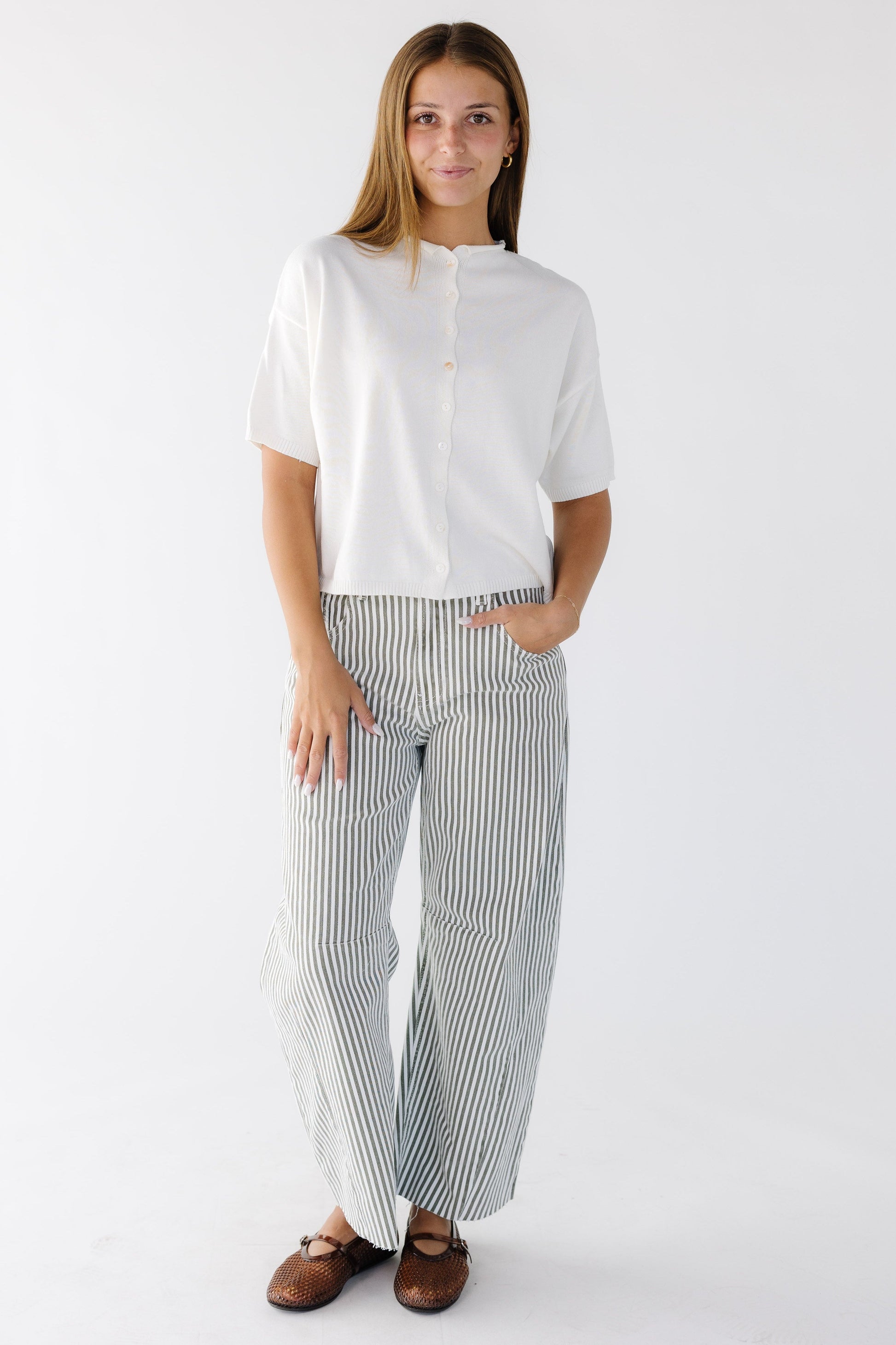 Woman wearing olive & white stripe barrel cut, wide leg pants paired with a white button down cardigan.