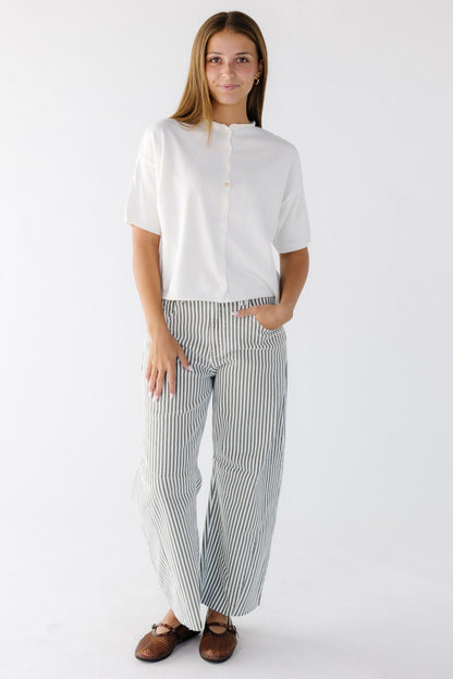 Woman wearing olive & white stripe barrel cut, wide leg pants paired with a white button down cardigan.