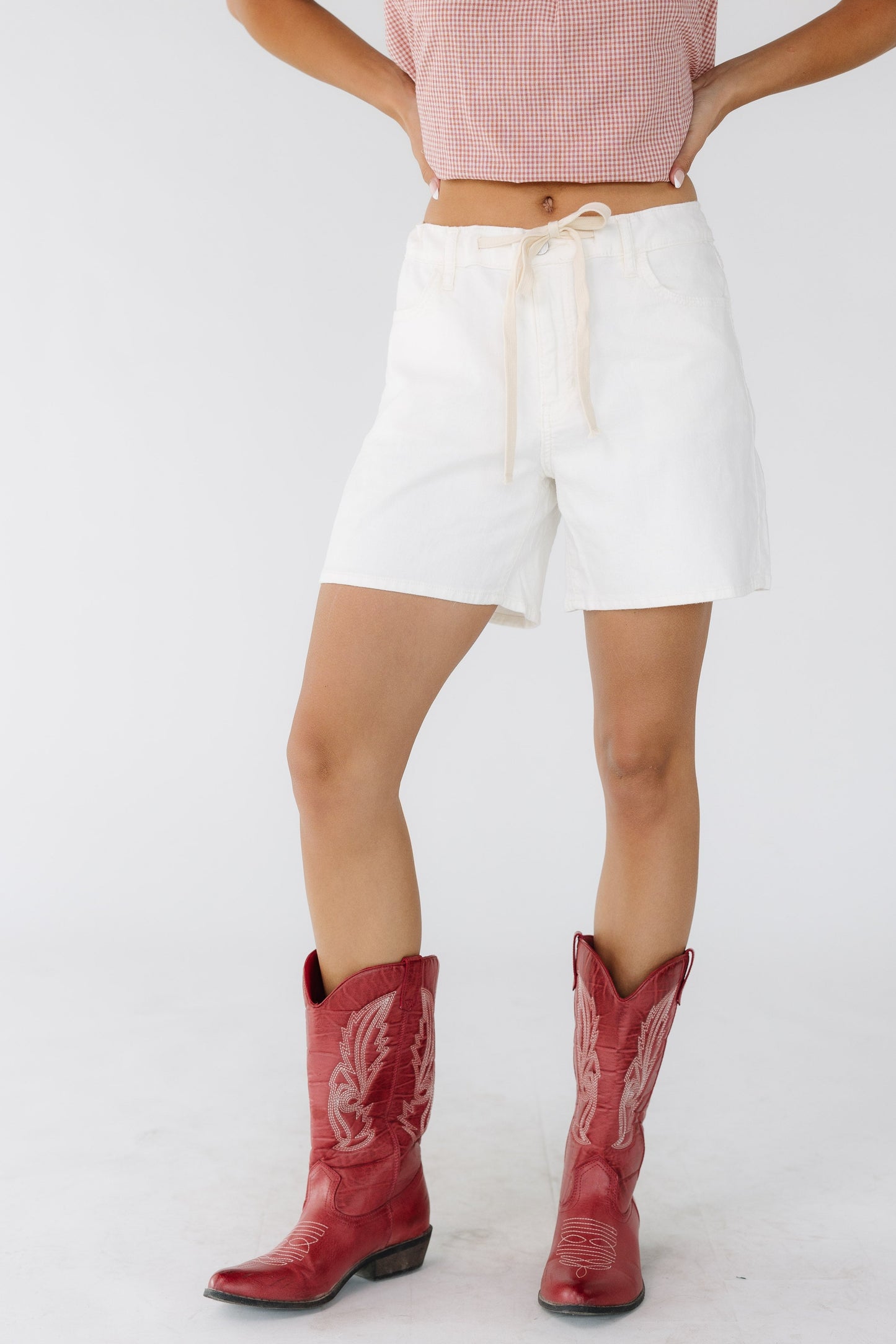 Young woman wearing off white shorts with a drawstring waist.