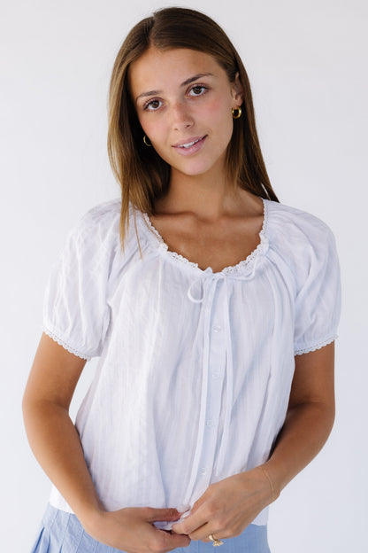 Young woman wearing a loose fitting white button down blouse witha lace trimmed scoop necline with a tie, and short lace trimmed puff sleeves.