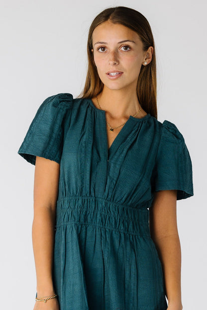 Close view of a woman wearing a teel dress with short sleeves and V-neckline