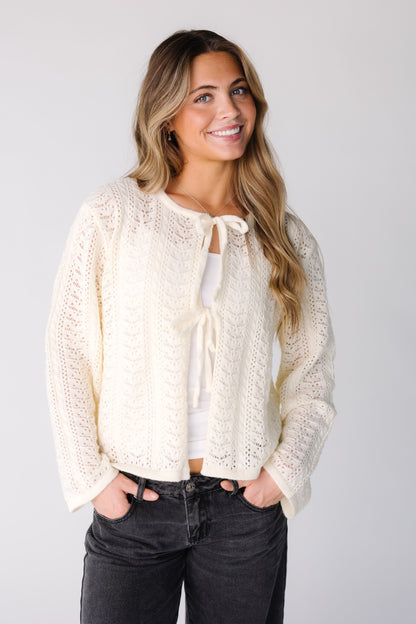 Woman wearing a cream long sleeve lace cardigan with 2 tie closure
