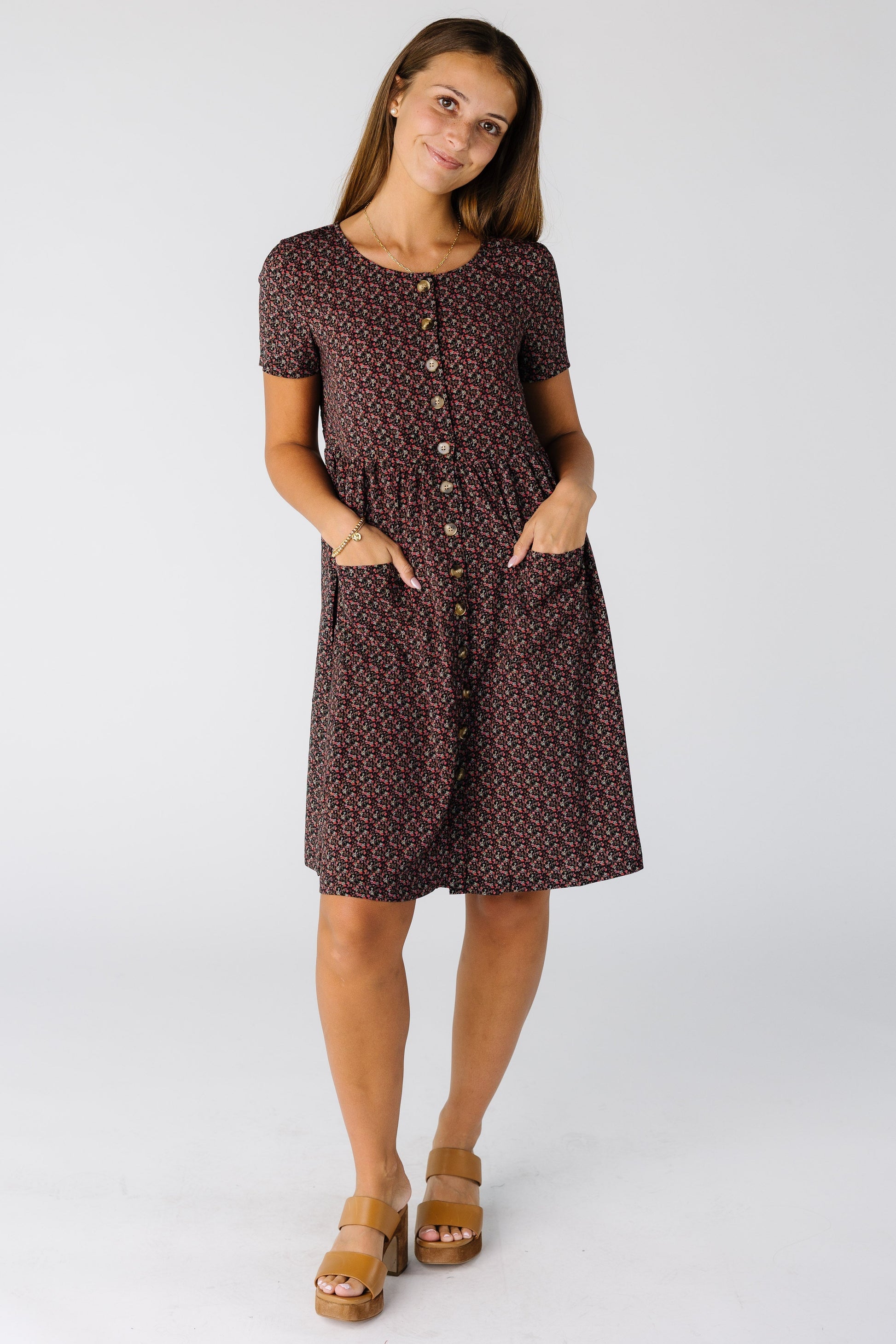 Woman wearing a modest floral print kne length dress with a slight scoop neckline, short sleeves and full button down dress