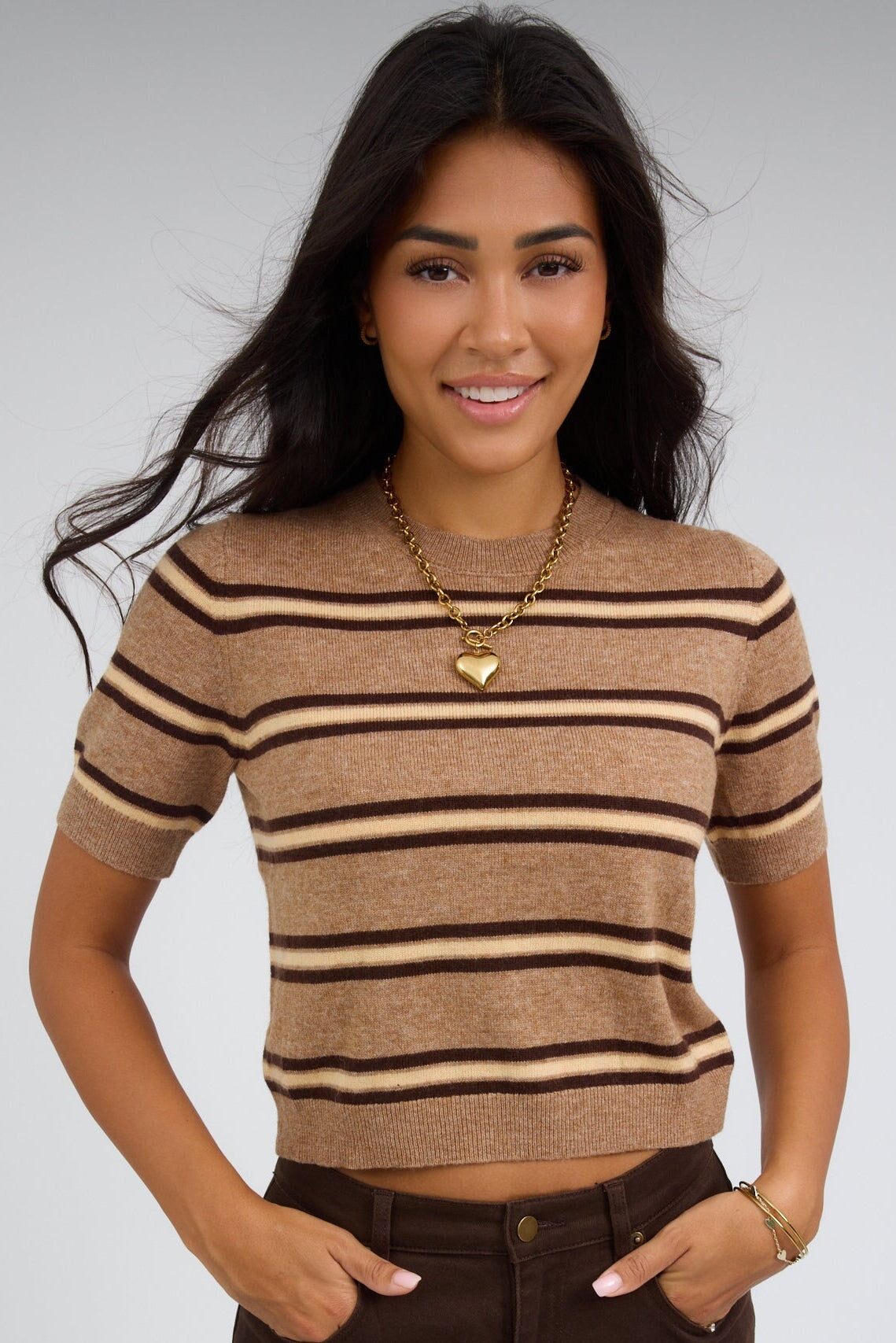 Young woman wearing a light brown stripe, lightweight stripe sweater with a round ribbed necklie and short sleeves.