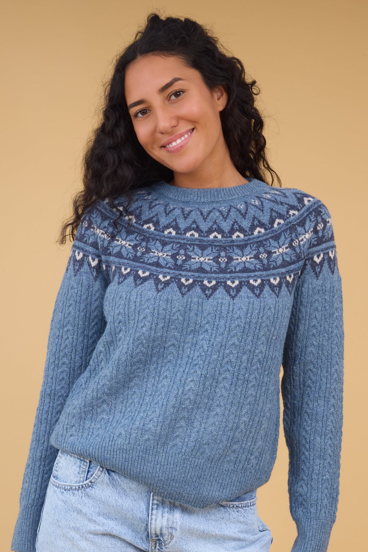 Young woman wearing a blue cable knit sweater with a nordic pattern yoke in blue & white.