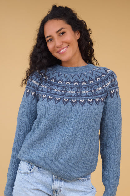 Young woman wearing a blue cable knit sweater with a nordic pattern yoke in blue & white.