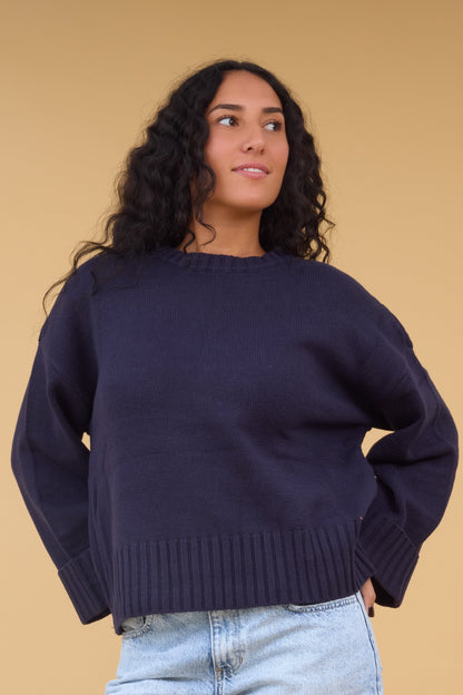 Young owman wearing a modest oversized navy sweater with extra wide ribbin at the cuffs & waist.