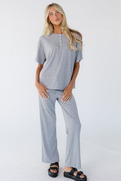 Woman wearing a grey loose fitting top with short sleeves and a short button placket.