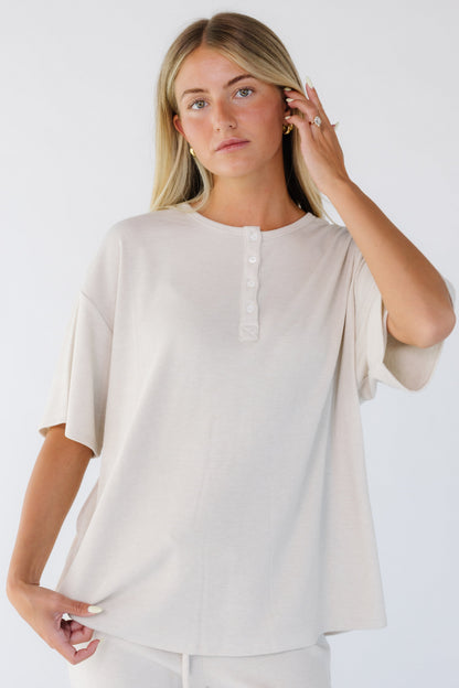 Young woman wearing a modest beige oversized top with short sleeves and a short button placket.