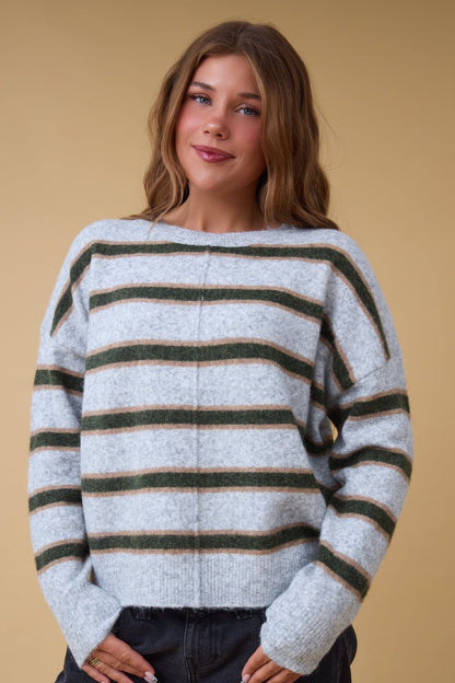 Young woman wearing a modest grey, green & gold stripe sweater with drop shoulders, long sleeves & ribbed waist & cuffs.