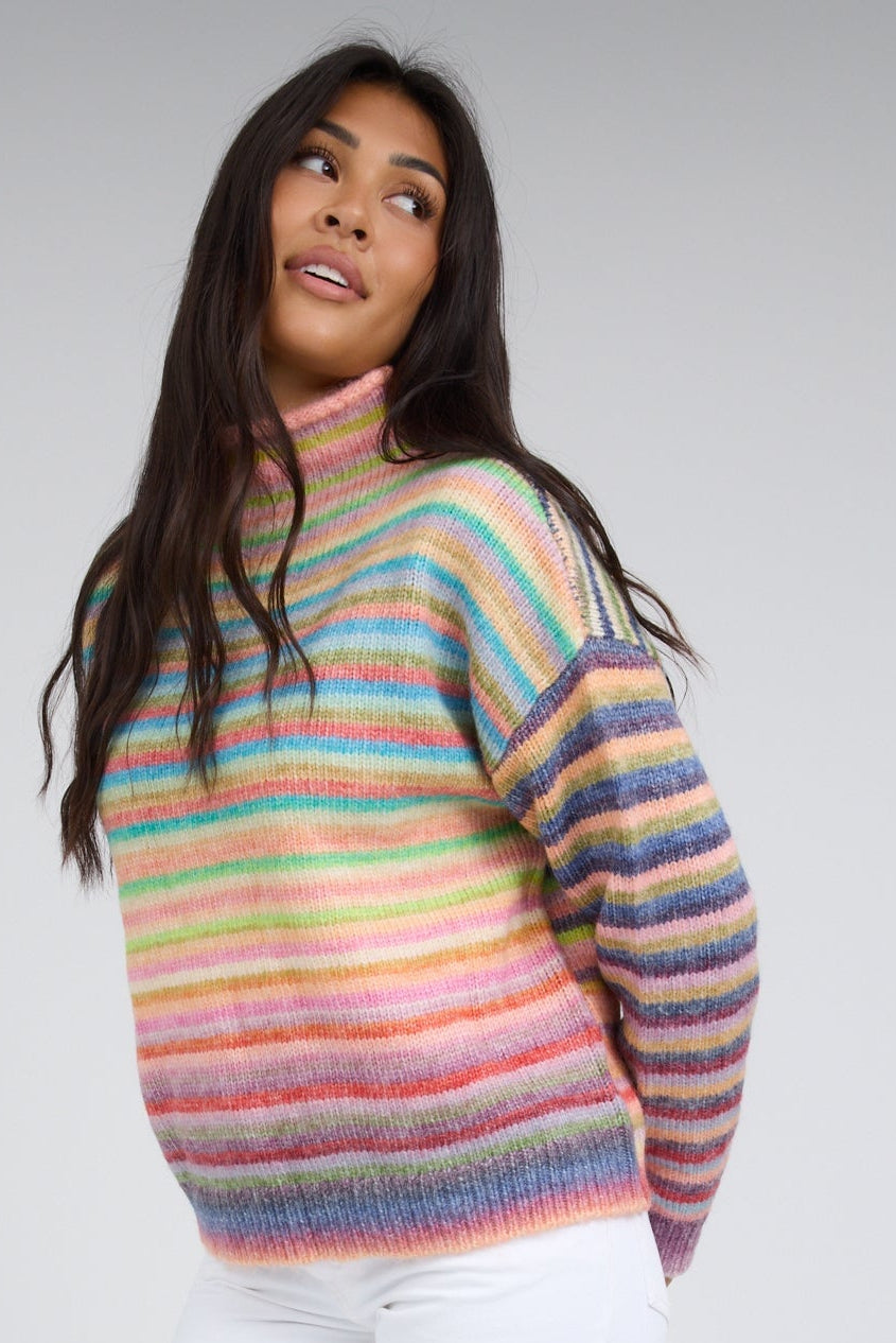 Young woman wearing a bright rainbow stripe sweater with long sleeves and a mock turtleneck.