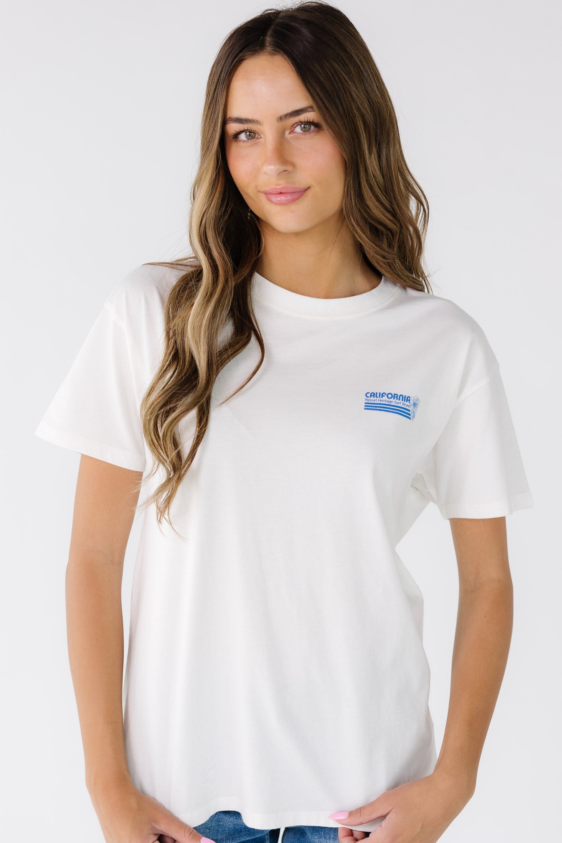 Woman wearing a white Rip Curl graphic tee with a small front graphic and short sleeves.