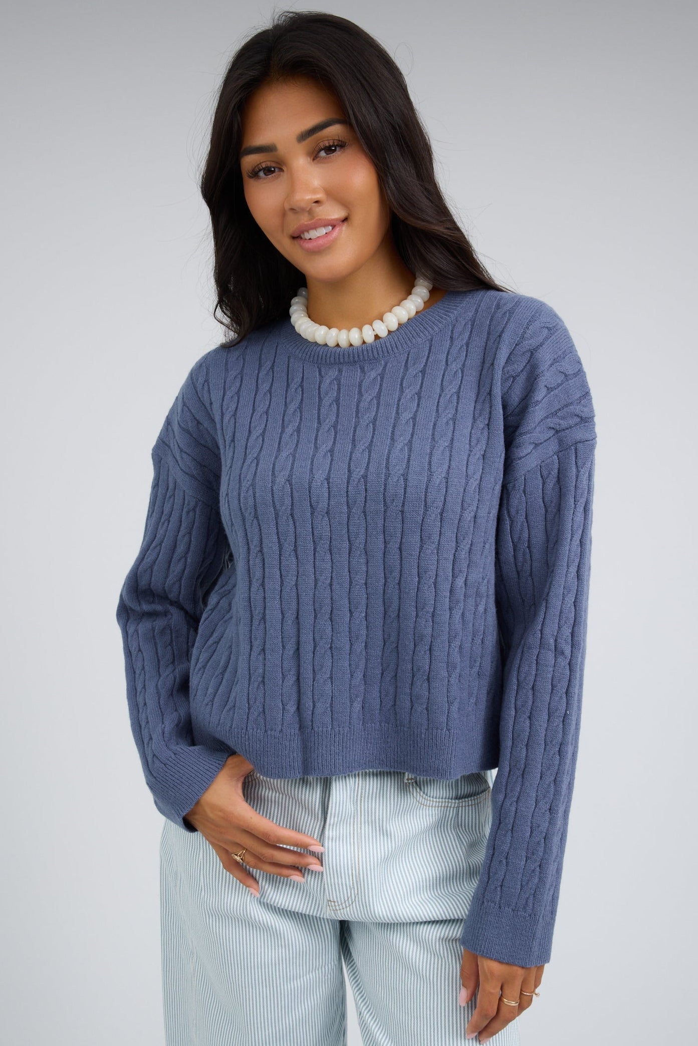 Young woman wearng a soft blue cable knit sweater with long sleeves.
