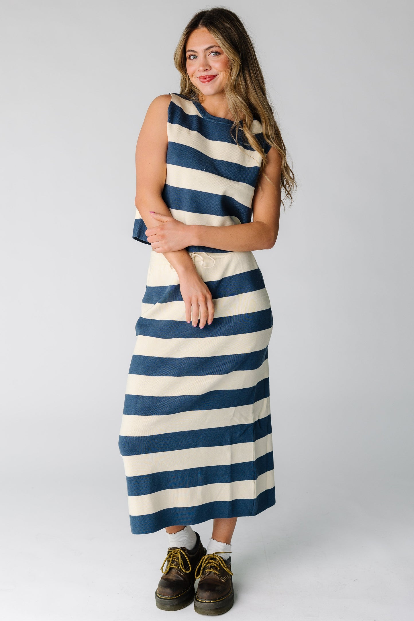 Woman wearing a blue and cream stripe knit  skirt and top matching set with a sleeveless top and round neckline with a midi length skirt.