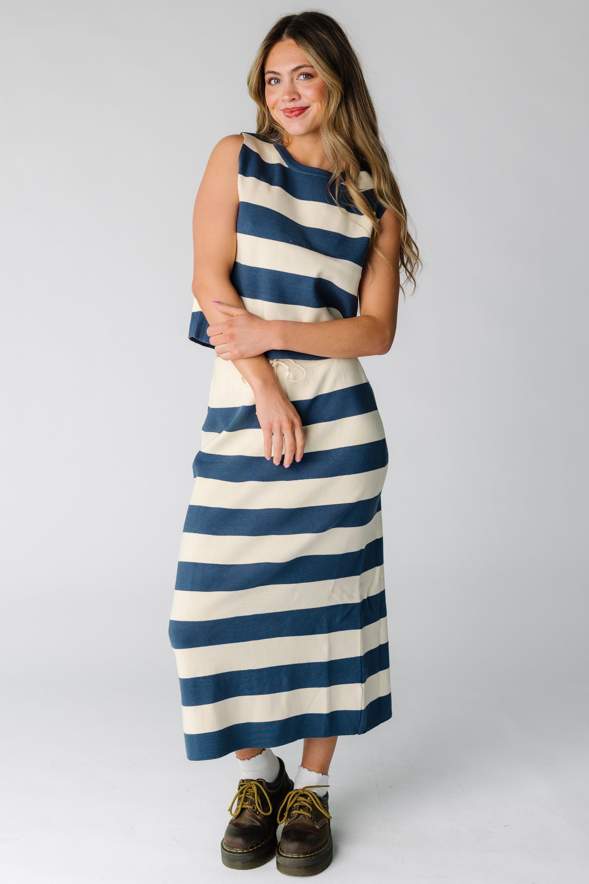 Woman wearing a blue and cream stripe knit  skirt and top matching set with a sleeveless top and round neckline with a midi length skirt.