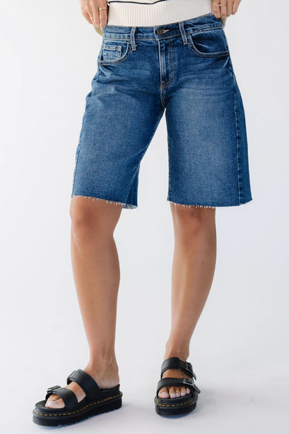 Young woman wearing a pair of knee length  dark denim shorts.