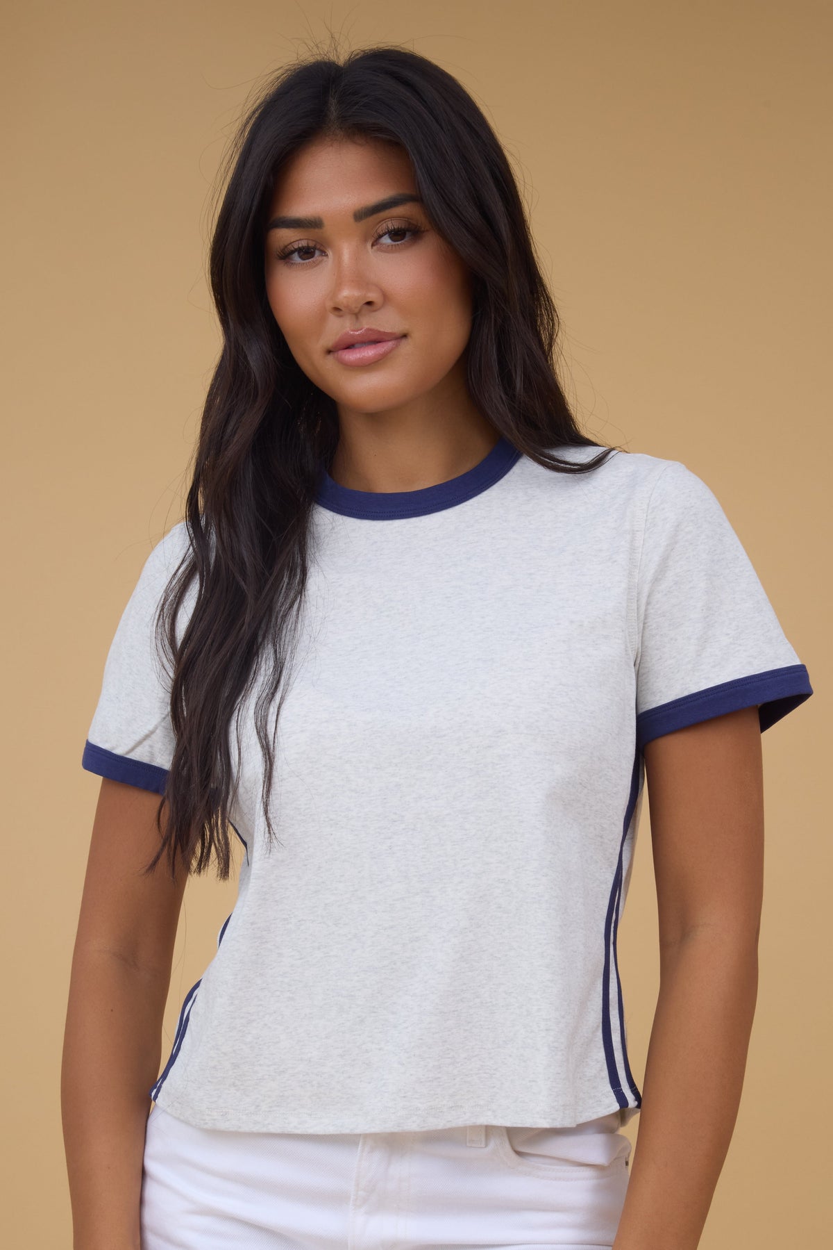 Woman wearing a closer fitting grey tee with a navy neckline and cuffs with double navy side stripes.