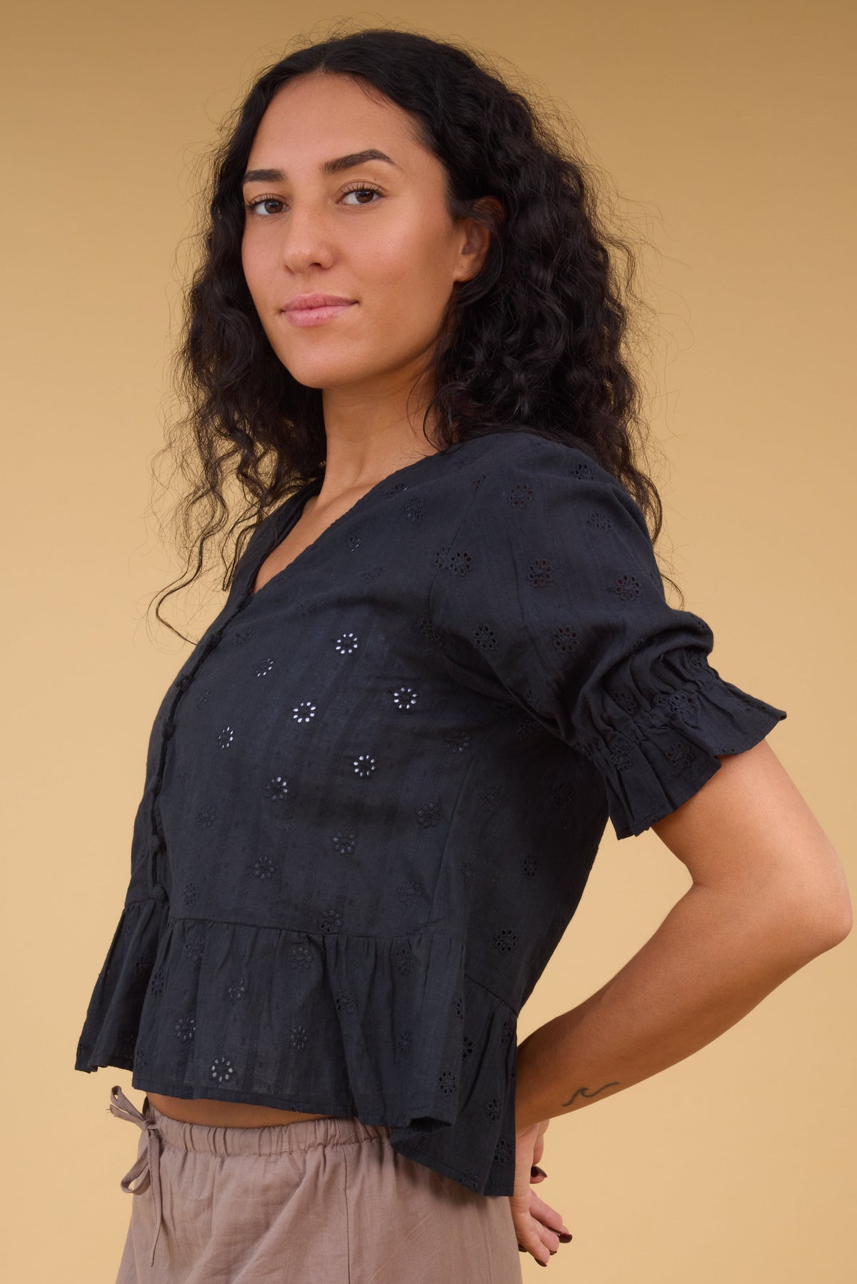 Side view of a woman wearing a black eyelet blouse witha  bottomruffle and short puff sleeves.