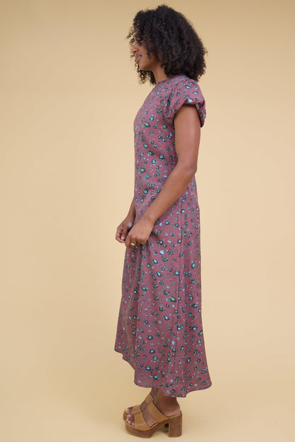 Side view of a woman wearing a magenta floral print midi dress with gathered cap sleeves.