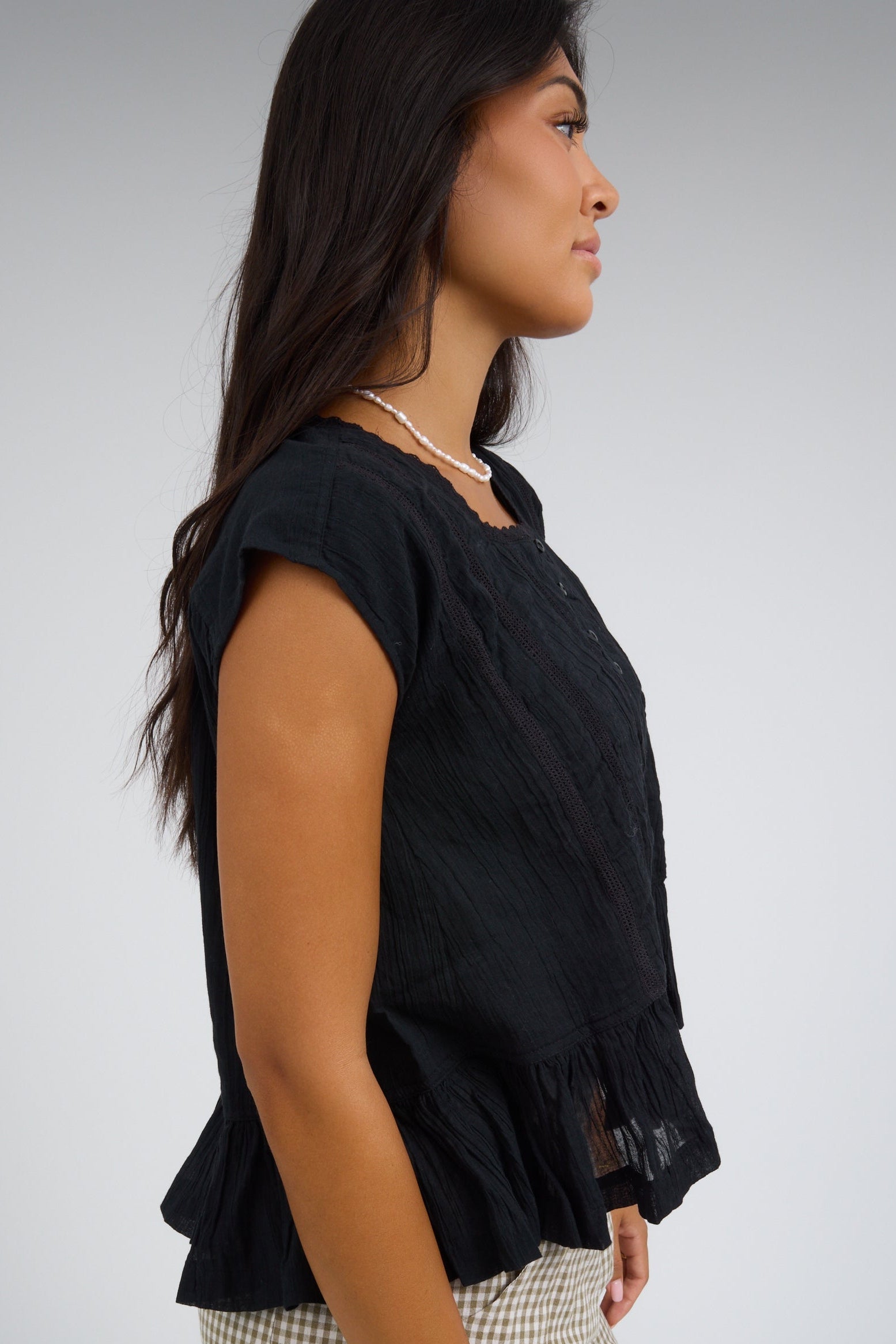 Side view of a woman wearing a black blouse with cap sleeves.