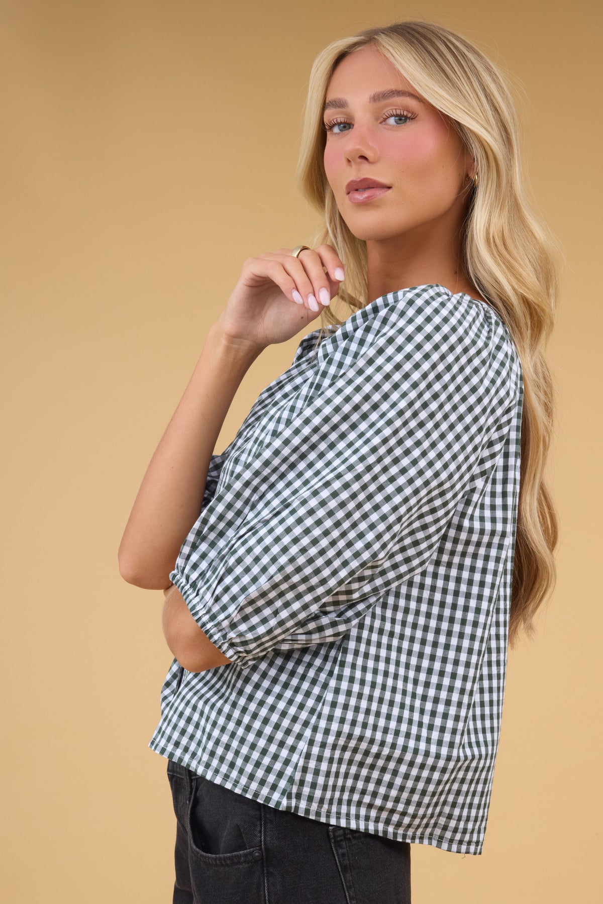 Side view of a woman wearing a green & white gingham blouse with half length sleeves.