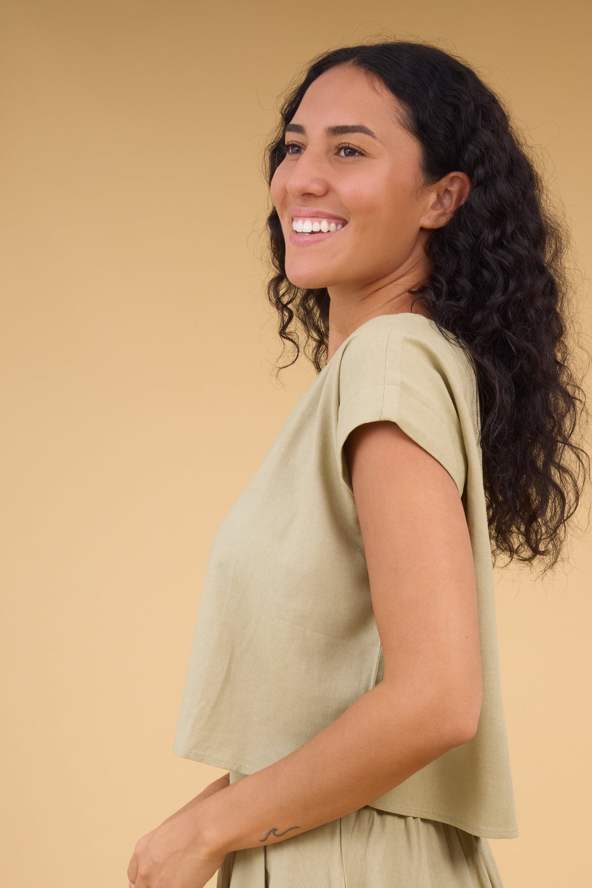 Side view of a woman wearing a light olive cap sleeve blouse.
