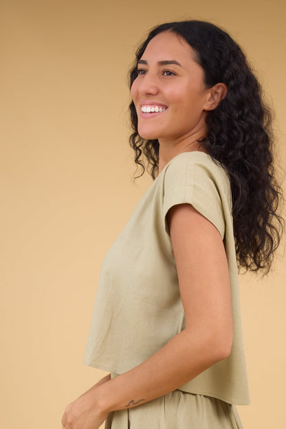 Side view of a woman wearing a light olive cap sleeve blouse.