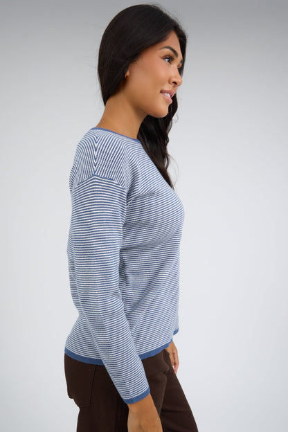 Side view of a woman wearing a texured blue & white stripe top with long sleeves.