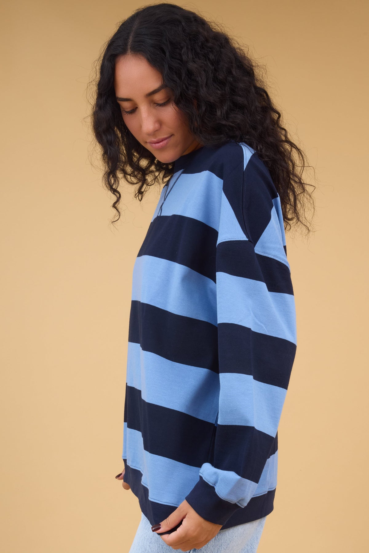 Side view of a woman wearing a light blue & navy wide stripe top with ribbed cuffs.