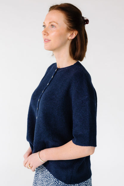 Side view of a young woman wearing a navy short sleeve cardigan.