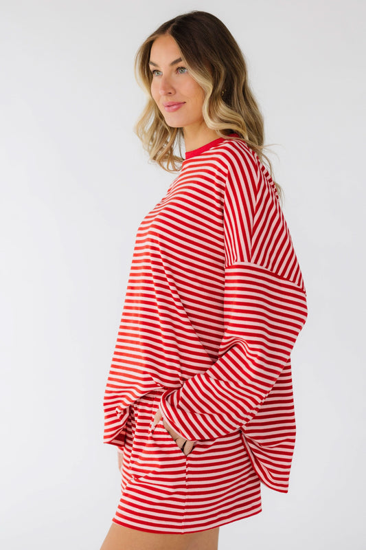 Young woman wearing a red & pink stripe short set with pockets, long sleeves and a crew neckline.