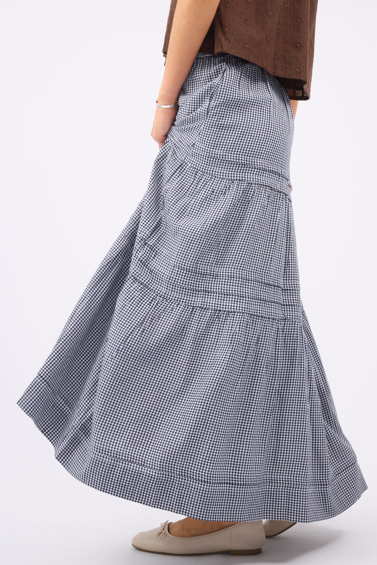 A woman wearing a navy & white gingham maxi skirt with folded pleats and tiers.