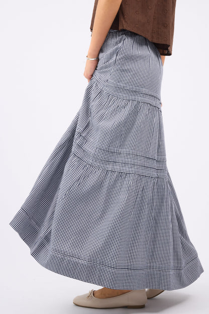 A woman wearing a navy & white gingham maxi skirt with folded pleats and tiers.