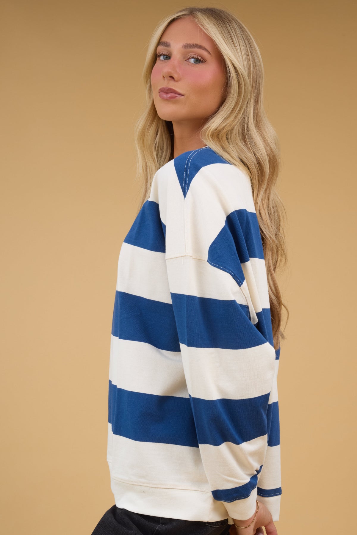 Woman wearing an ivory and blue wide stripe knit wop with drop shoulders and long sleeves.