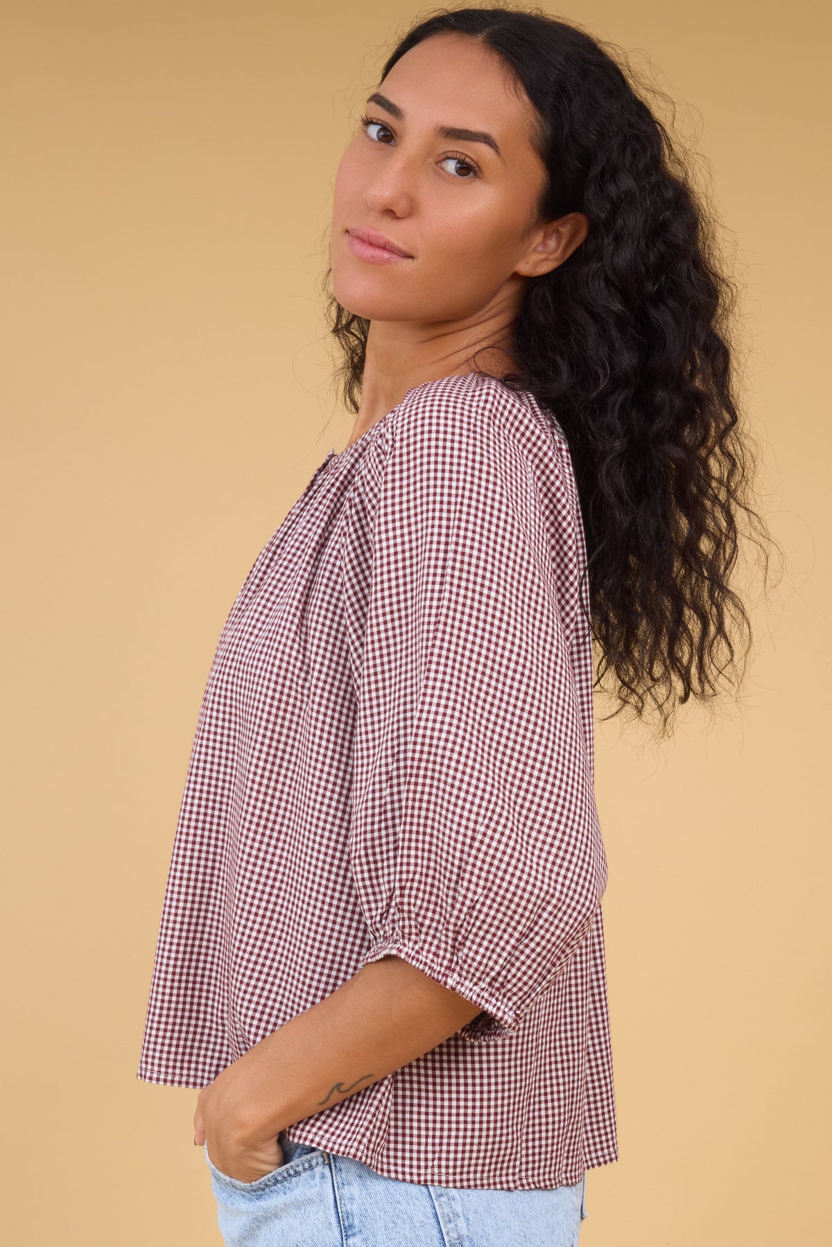 Side view of a woman wearing a burgugndy gingham blouse with half length sleeves.