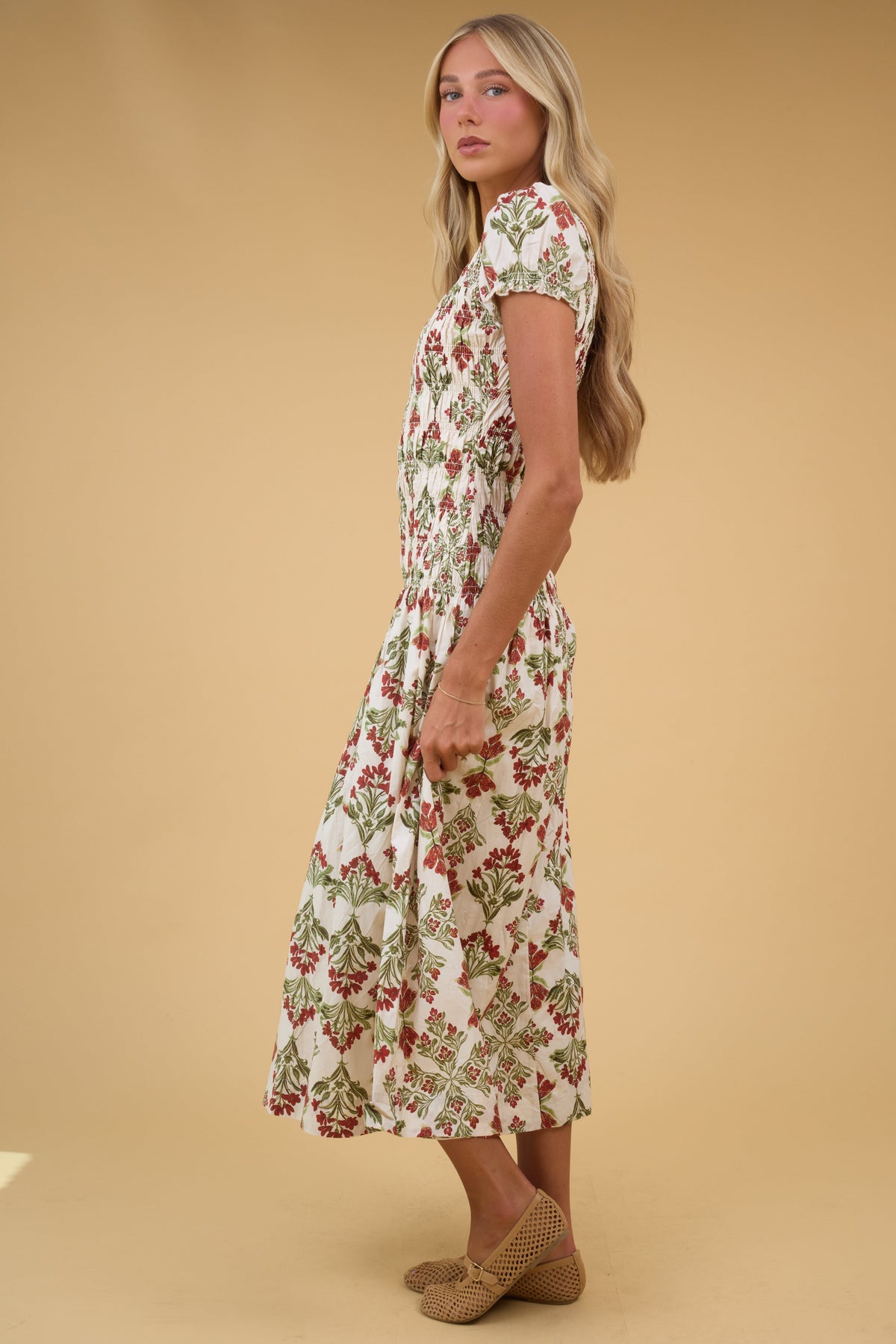 Side view of a young woman wearing a cream floral midi dress with a smocked bodice and short puff sleeves.