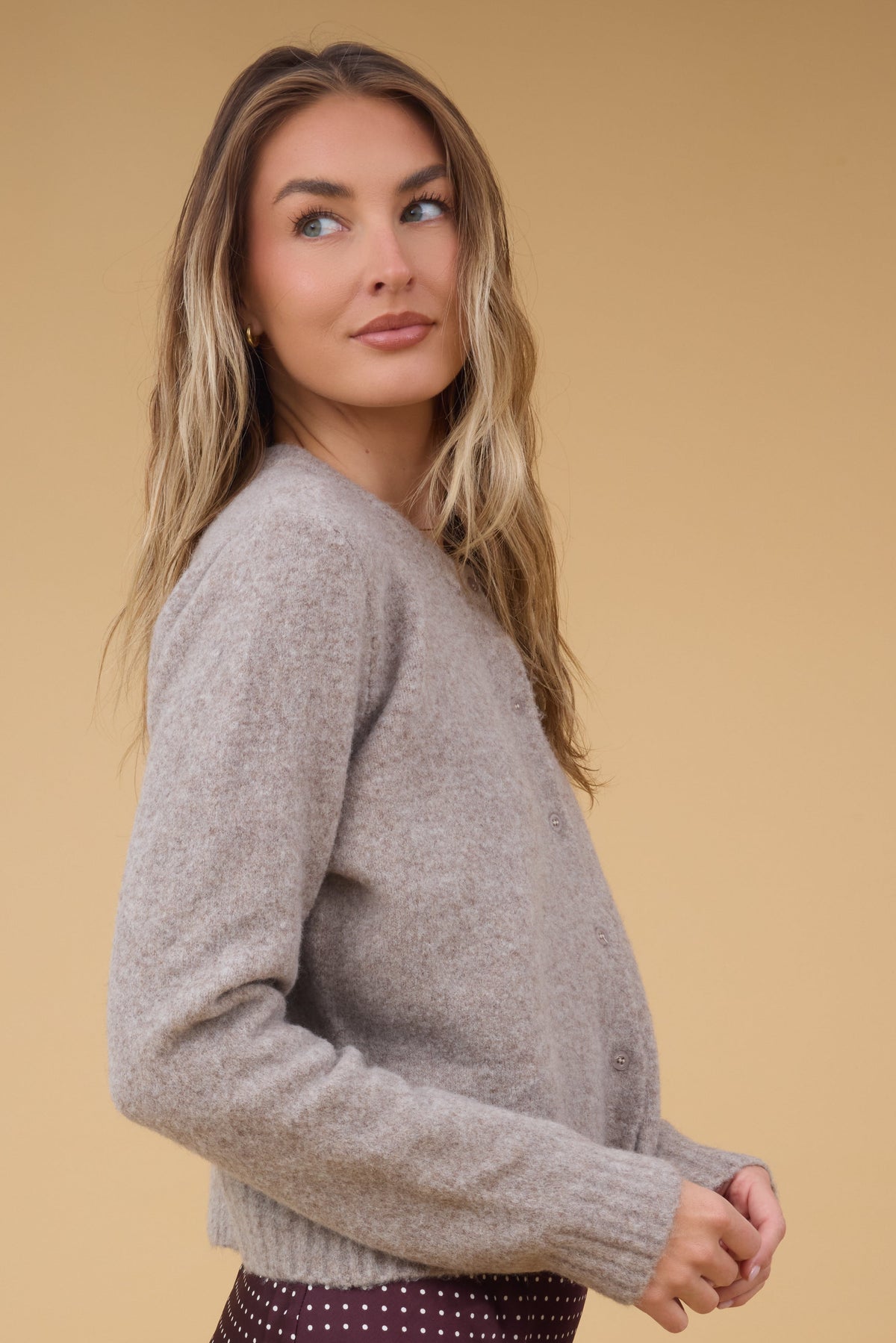 A side view of a woman wearing beige log sleeve cardigan with matching buttons.