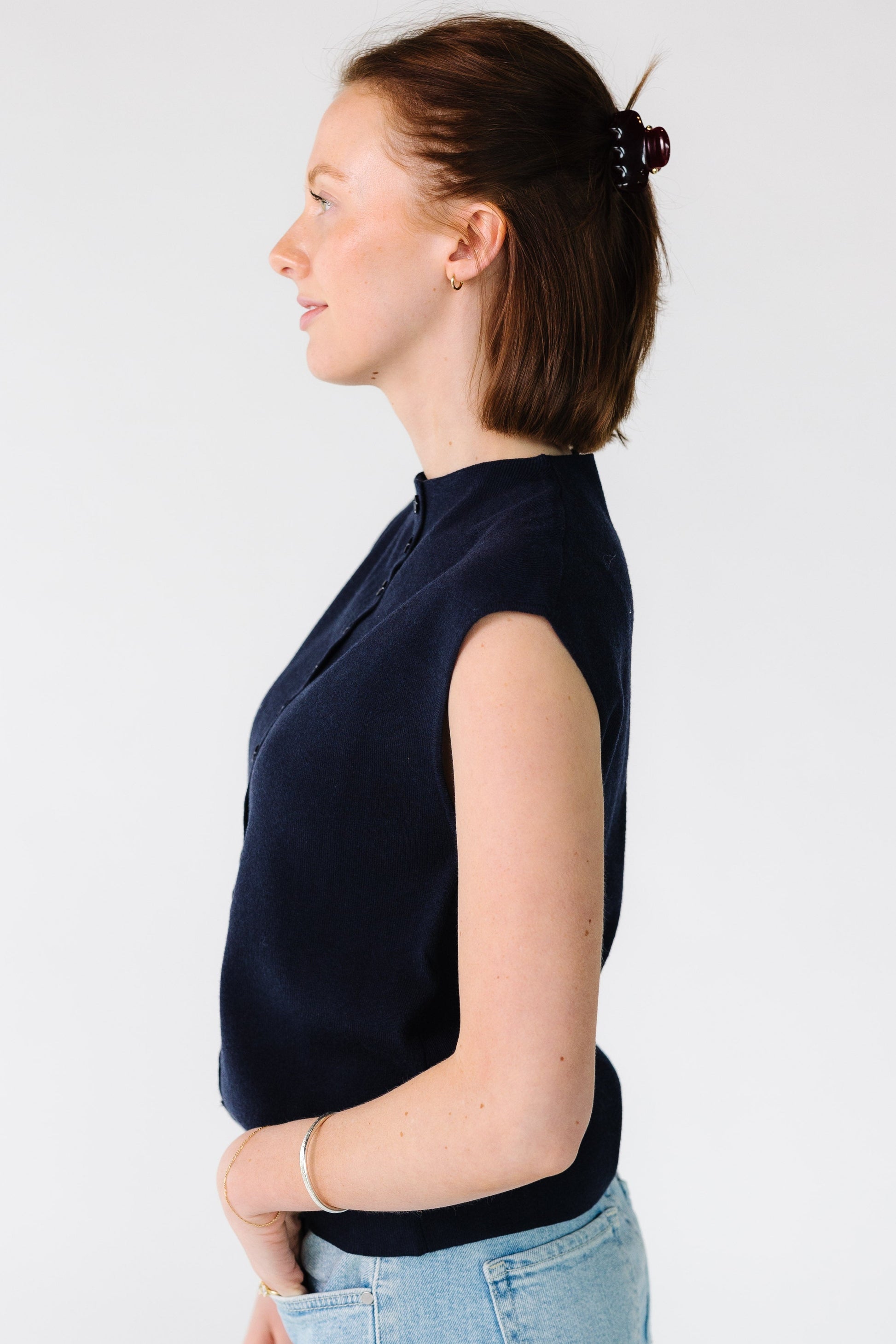 Side view of a woman wearing a navy button down, sleeveless sweater vest.