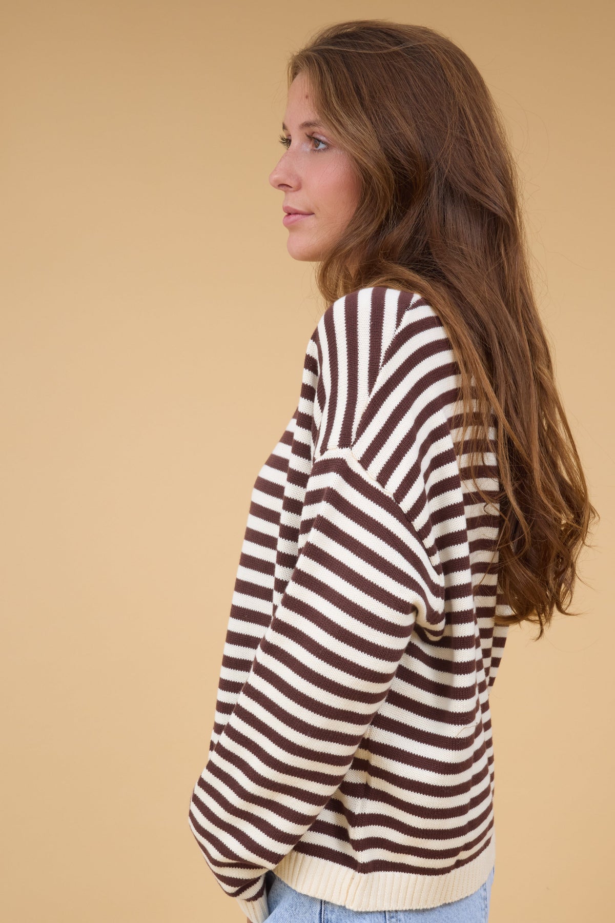 A side view of a woman wearing a loose fitting brown & cream stripe knit top with long sleeves.