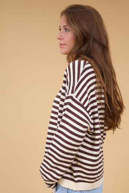 A side view of a woman wearing a loose fitting brown & cream stripe knit top with long sleeves.