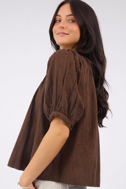 A side view of a woman wearing a brown eyelet blouse with puff sleeves.