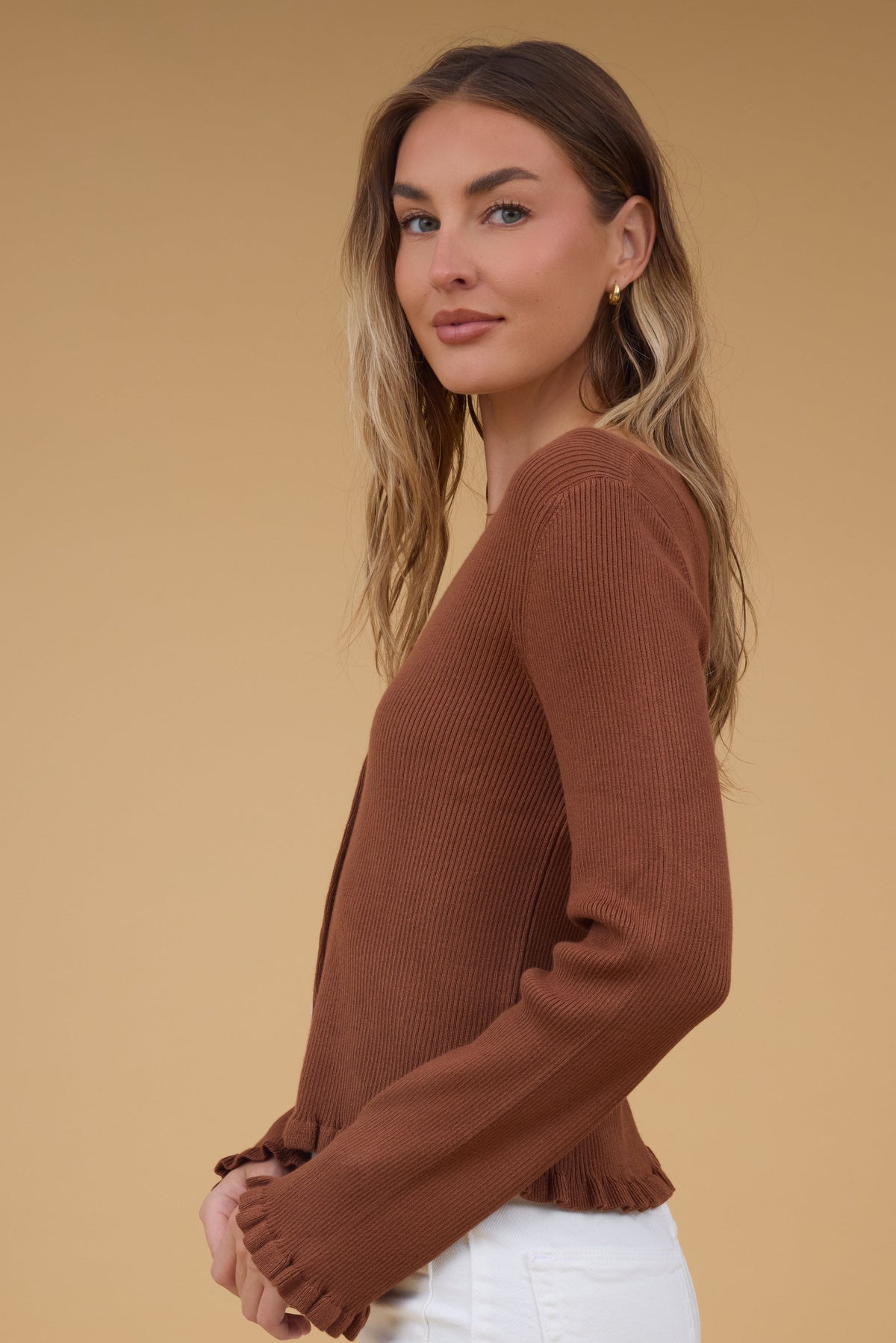 Side view of a woman wearing a soft rib knit top with long sleeve  and ruffles at the cuffs and waist.