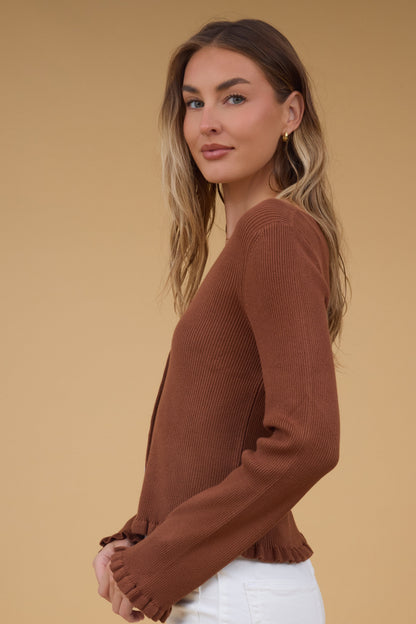 Side view of a woman wearing a soft rib knit top with long sleeve  and ruffles at the cuffs and waist.